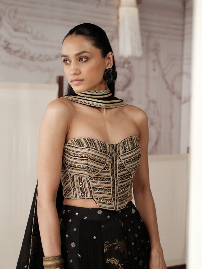 Black And Gold Banarasi lehenga choli featuring intricate gold embroidery, delicate motifs and a richly detailed border, paired with a matching embellished dupatta. It also features a modern strapless corset blouse.